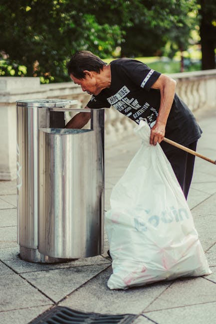 In the image, a collection of discarded household items is arranged outdoors on a paved driveway, likely for rubbish removal. The foreground features a stack of various objects, including cardboard bo